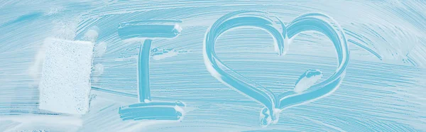 Colpo panoramico di pulitore con spugna vicino amo lettering scritto a mano su vetro con schiuma bianca su sfondo blu — Foto stock