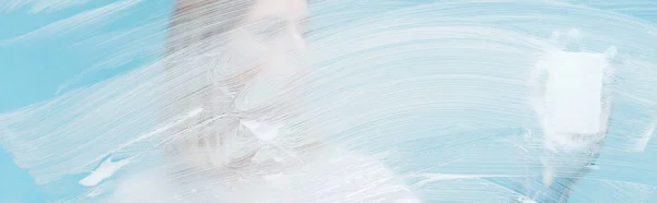 Plan panoramique de la femme avec éponge derrière le verre avec mousse blanche sur fond bleu — Photo de stock