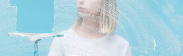 Panoramic shot of young woman leaning glass with squeegee on blue background — Stock Photo