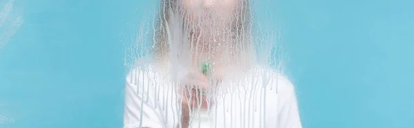 Панорамный снимок молодой женщины чистящего стекла с капающим моющим средством на синем фоне — стоковое фото