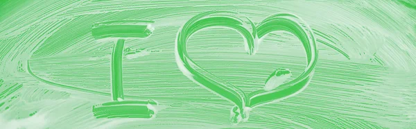 Panoramaaufnahme von Glas mit weißem Schaumstoff auf grünem Hintergrund mit i-Buchstabe und Herzschild — Stockfoto