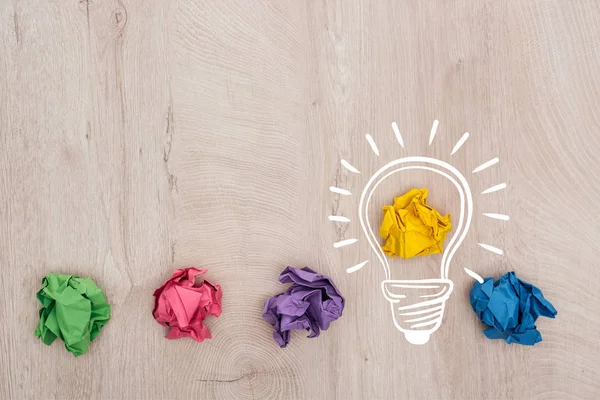 Vue de dessus des boules de papier froissées multicolores et illustration d'ampoule sur la surface en bois, concept d'entreprise — Photo de stock