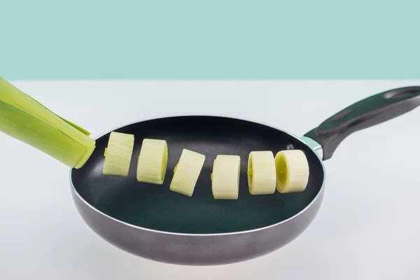 Poireau vert haché dans une casserole sur surface blanche isolé sur turquoise — Photo de stock