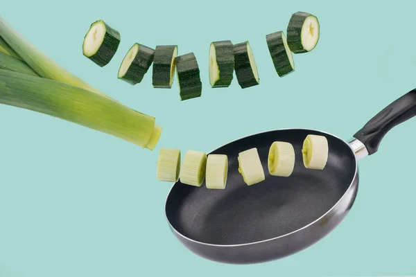 Нарезанные зеленые свежие цуккини и лук-порей над сковородой, изолированные на бирюзовой — стоковое фото