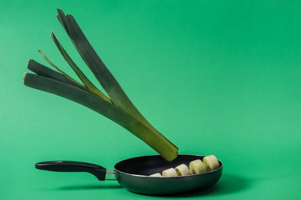 Зеленый свежий вкусный лук-порей в сковороде на зеленом фоне — стоковое фото
