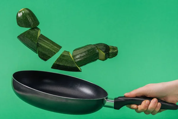 Обрезанный вид женщины, держащей сковородку с зеленым рубленым цуккини изолированы на зеленый — стоковое фото