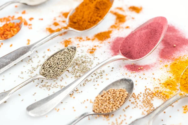 Close up view of various bright spices in silver spoons on white background — Stock Photo