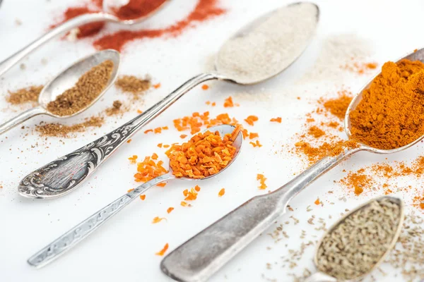 Close up view of various colorful spices in silver spoons on white background — Stock Photo