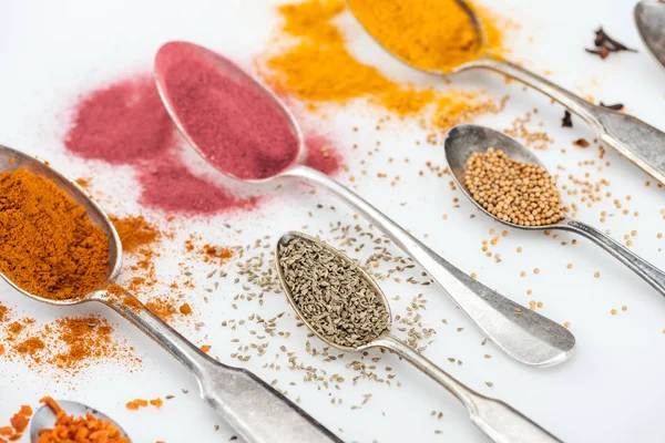 Close up view of various spices in silver spoons on white background — Stock Photo