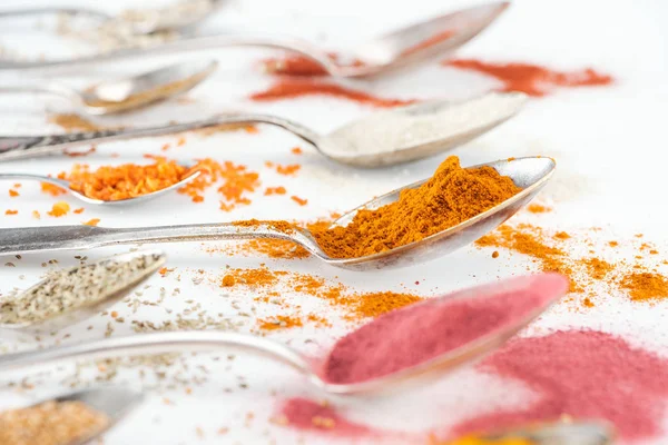 Selective focus of colorful bright spices in silver spoons on white background — Stock Photo