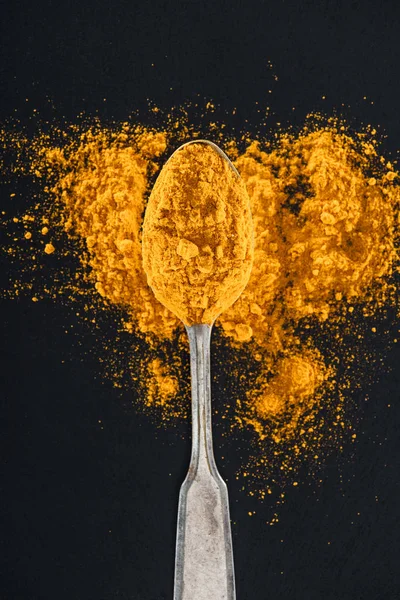 Vista dall'alto del curry in polvere in cucchiaio d'argento su sfondo nero — Foto stock