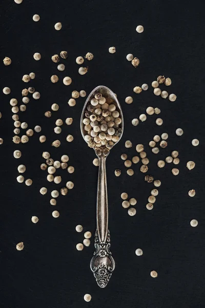 Vue du dessus du poivre blanc dans une cuillère en argent sur fond noir — Photo de stock