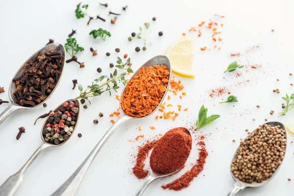 Close up view of indian bright spices in silver spoons near herbs on white background — Stock Photo