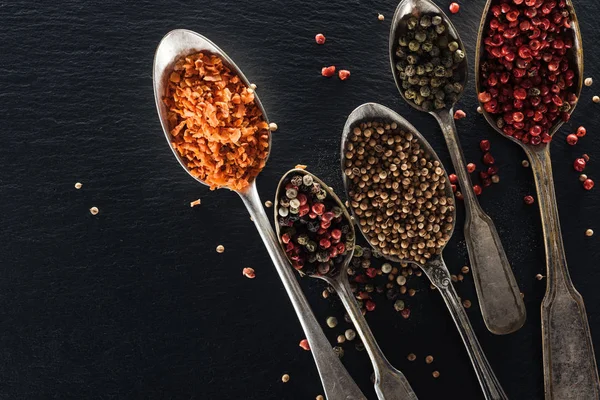 Top view of pepper, candied fruit and mustard in silver spoons on black textured background — Stock Photo