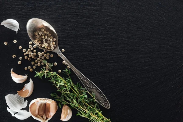 Top view of white pepper in silver spoon near garlic cloves and green herb — Stock Photo
