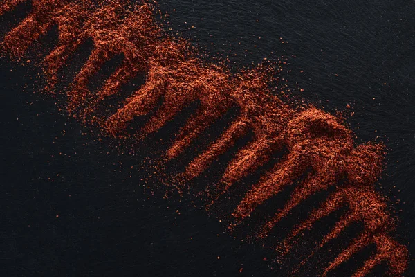 Top view of red pepper powder scattered on black background — Stock Photo