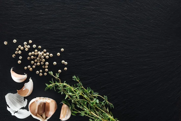 Top view of white pepper on black background near garlic cloves and thyme — Stock Photo