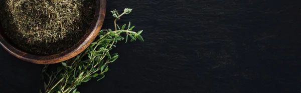 Panoramic shot of dried thyme in wooden bowl near green herb on black background — Stock Photo