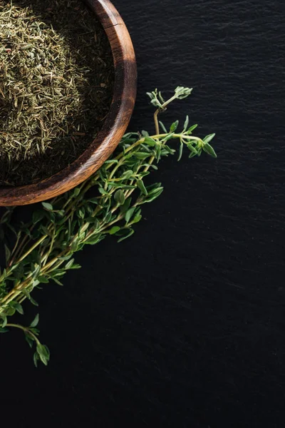 Top view of dried thyme in wooden bowl near green herb on black background — Stock Photo