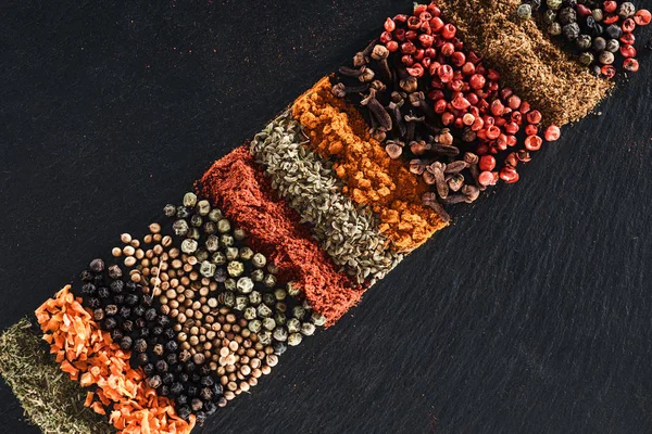 Vista superior de especiarias tradicionais indianas brilhantes e frutas secas sobre fundo preto texturizado — Fotografia de Stock