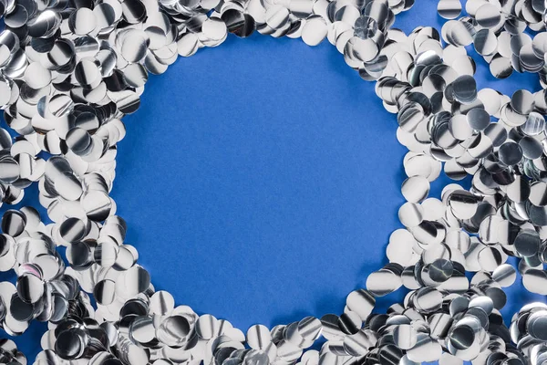 Top view of silver circle made of confetti on blue background — Stock Photo