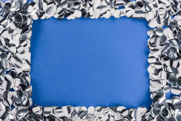 Top view of silver confetti frame on blue background — Stock Photo