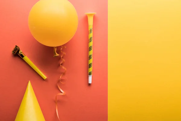 Top view of yellow balloon, streamer, party hat on coral and yellow background — Stock Photo