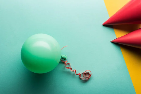 Vista superior de globos verdes y sombreros rojos de fiesta sobre tiffany y fondo amarillo - foto de stock