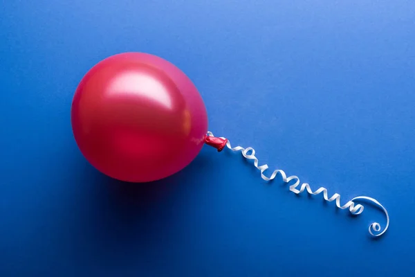 Draufsicht auf roten Ballon mit weißer Luftschlange auf blauem Hintergrund — Stockfoto