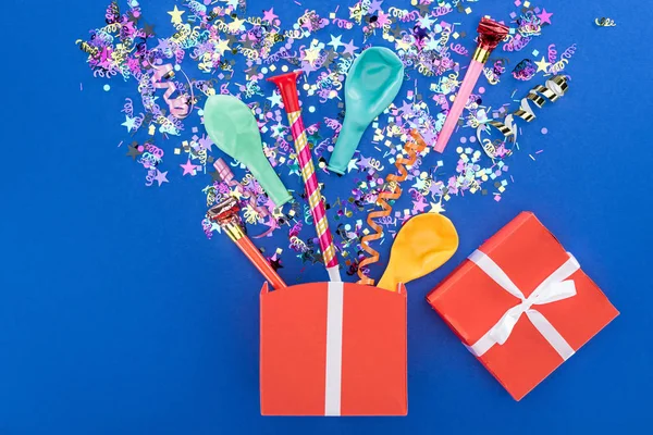 Red gift box and various party decor on blue background — Stock Photo