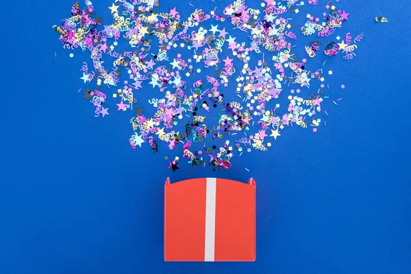 Vista superior de la caja de regalo con confeti brillante brillante sobre fondo azul - foto de stock