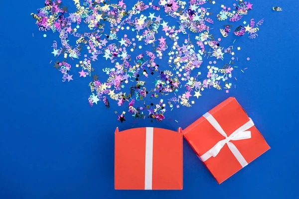 Rote Geschenkschachtel und buntes, glänzendes Konfetti auf blauem Hintergrund — Stockfoto