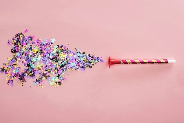 Cuerno de fiesta y confeti multicolor sobre fondo rosa - foto de stock