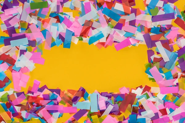 Vue du dessus du cadre confetti multicolore sur fond jaune avec espace de copie — Photo de stock