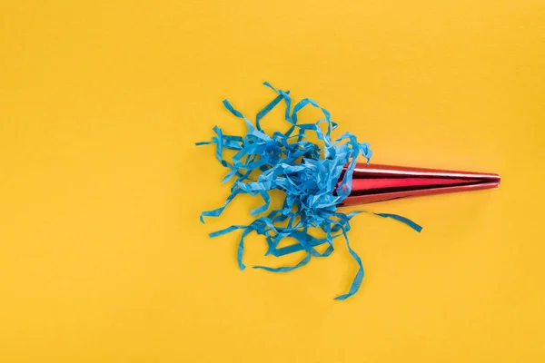 Vue du dessus de corne de fête rouge avec confettis en papier bleu sur fond jaune — Photo de stock