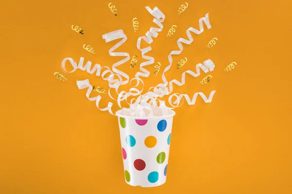 White and golden ribbons in polka dot cup on orange background — Stock Photo