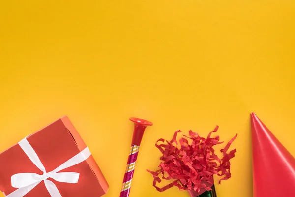 Vue du dessus de la boîte cadeau rouge, corne de fête et chapeau de fête sur fond jaune — Photo de stock