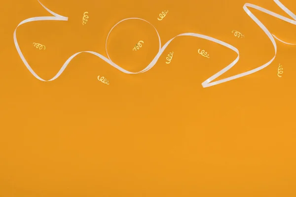 Top view white ribbon and golden confetti on orange background — Stock Photo
