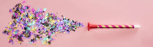 Panoramic shot of party horn with sparkling confetti on pink background — Stock Photo