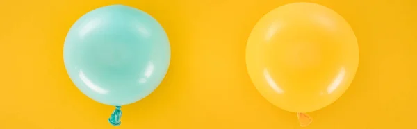 Panoramic shot of blue and yellow balloons on yellow background — Stock Photo