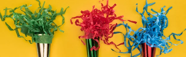 Panoramic shot of multicolored party horns on yellow background — Stock Photo