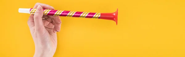 Panoramic shot of woman holding red party horn on yellow background — Stock Photo