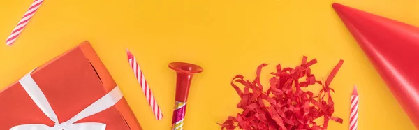 Panorâmica tiro de caixa de presente vermelho, velas e chifre de festa no fundo amarelo — Fotografia de Stock