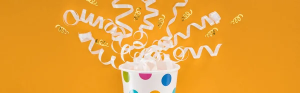 Panoramic shot of white ribbons and polka dot paper cup on orange background — Stock Photo