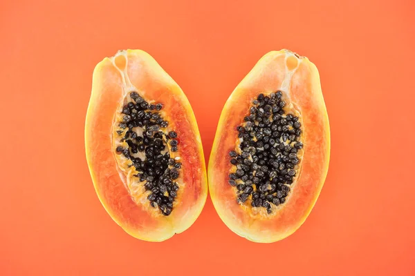 Top view of ripe bright papaya halves with black seeds isolated on orange — Stock Photo