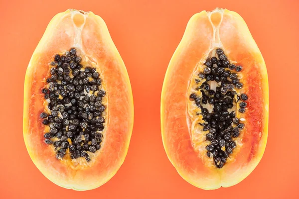 Vista superior de mitades maduras de papaya exótica con semillas negras aisladas en naranja - foto de stock