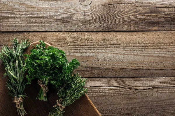 Top view of green rosemary, parsley and thyme on chopping board on wooden weathered table with copy space — Stock Photo