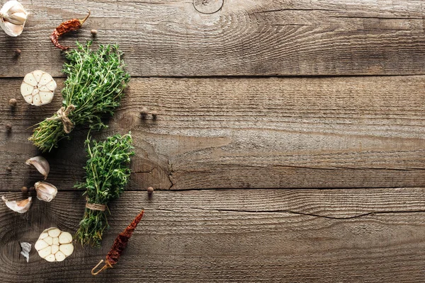 Top view of green thyme, dried chili peppers, garlic cloves and black pepper on wooden weathered table with copy space — Stock Photo