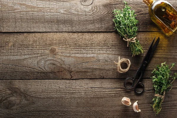 Top view of vintage scissors near green thyme, garlic cloves and oil in bottle on wooden brown table — Stock Photo