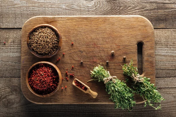 Top view of green thyme on wooden chopping board with coriander and pink peppercorn in bowls — Stock Photo